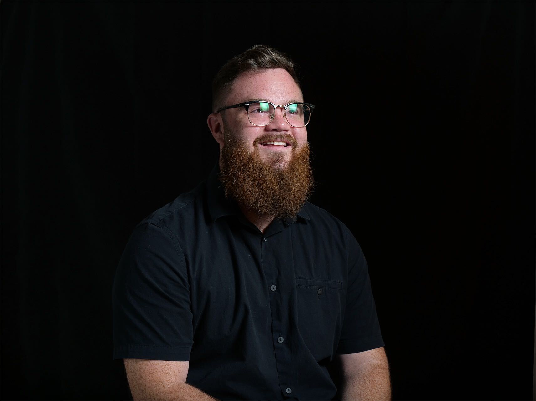 Matt Ward smiling, wearing glasses and a black shirt against a dark background